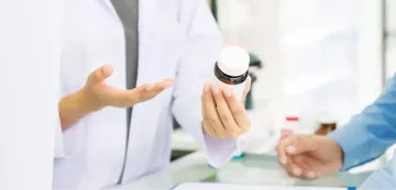 Ein Arzt hält eine Medikamentenflasche in der Hand, während er in einer Klinik mit einem Patienten spricht.