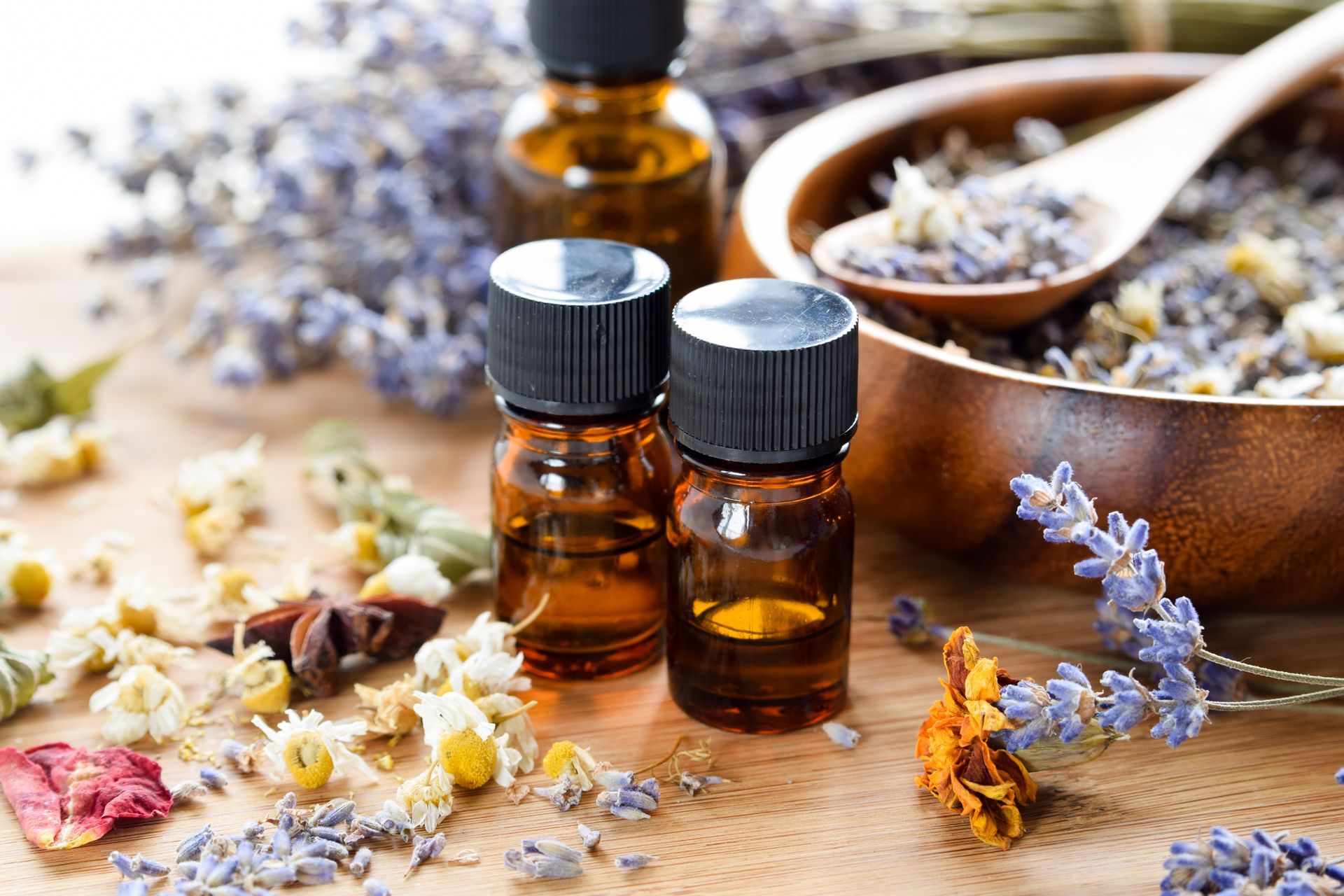 Kleine, bernsteinfarbene Fläschchen mit ätherischen Ölen, Lavendel und getrockneten Blüten auf einem rustikalen Holztisch