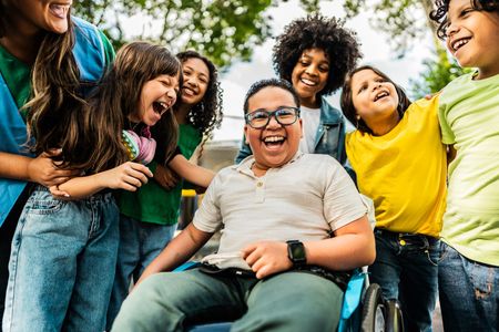 A group of happy children are standing around a smiling boy in a wheelchair.