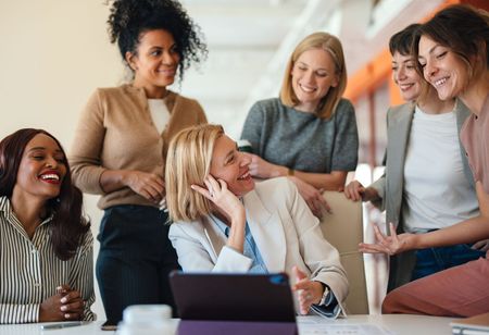 A group of women are sitting around a table looking at a tablet.