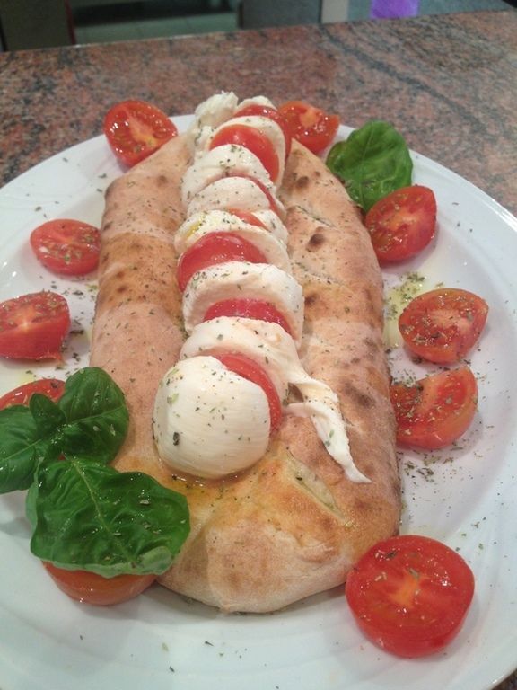 Una pizza con pomodori e mozzarella su un piatto bianco.