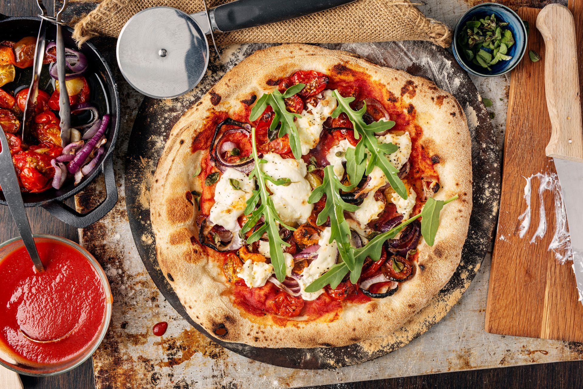 Una pizza è appoggiata su un tagliere accanto a una rotella tagliapizza.