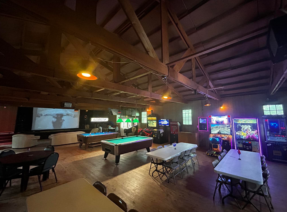 A large room with pool tables , tables , chairs and arcade games.