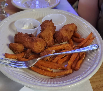 A white plate topped with fried fish and sweet potato fries with a fork.