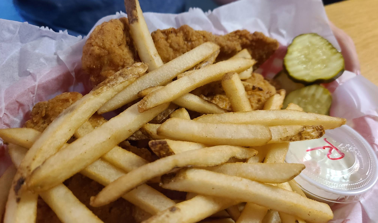 A basket of fried chicken and french fries with a pickle and dipping sauce.