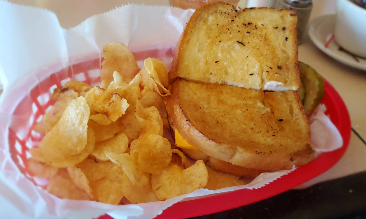 A grilled cheese sandwich and potato chips in a basket on a table.