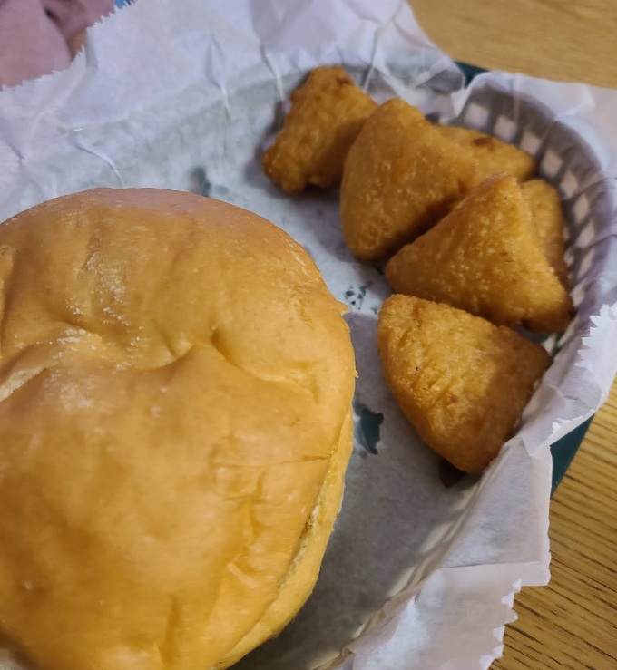 A bun and some fried food in a basket on a table