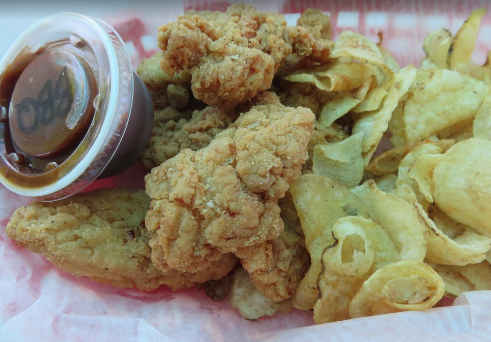 A close up of fried chicken and chips with a dipping sauce
