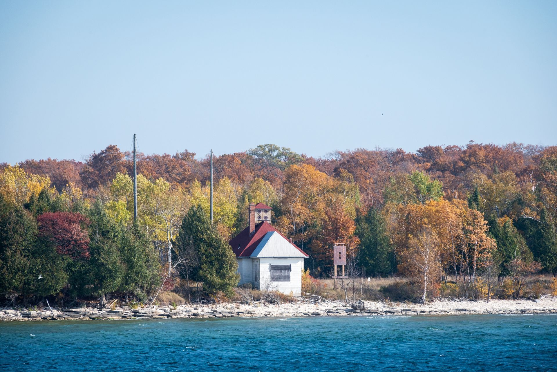 A small white house with a red roof is sitting on the shore of a lake surrounded by trees.