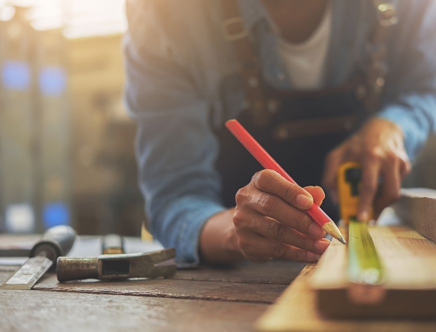 A person is measuring a piece of wood with a tape measure and a pencil