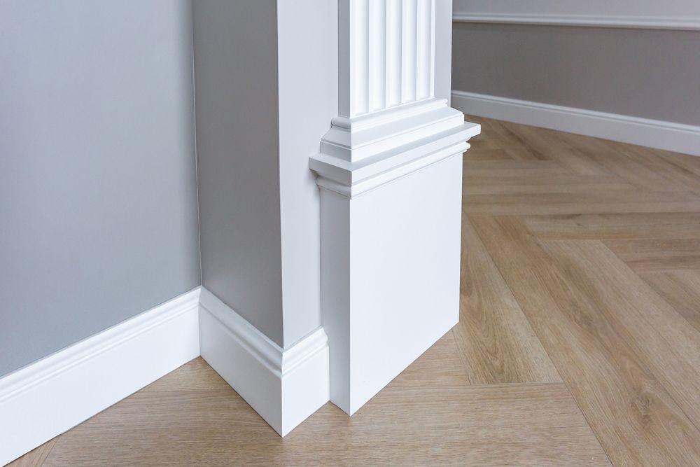 A corner of a room with white molding and a wooden floor