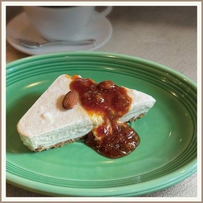 緑の皿の上にキャラメルソースをかけたチーズケーキのスライスと、背景にコーヒーカップ。