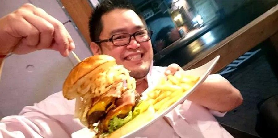 Man holding up a plate with a tall hamburger and fries.