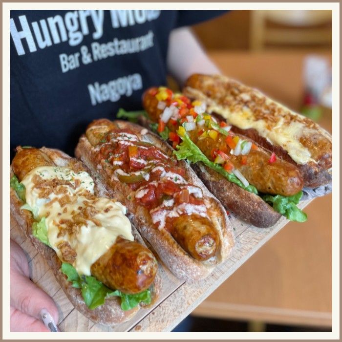 Restaurant staff holding a tray of gourmet hotdogs.