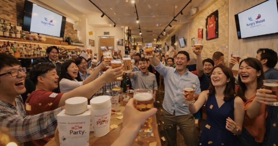 People toasting beer glasses in a bar, confetti falling.