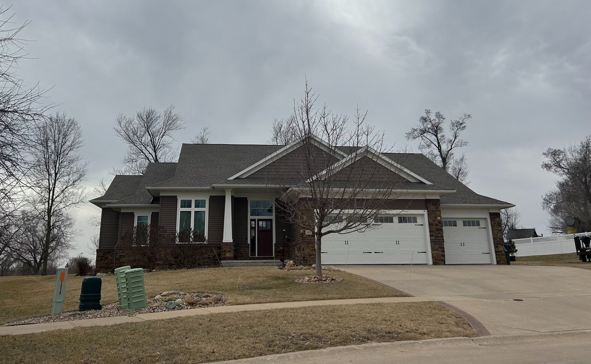 A one-story brick home with a gray roof and a two-car garage under a cloudy sky.