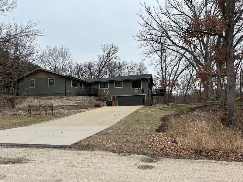 Green house with a long driveway on a hill, surrounded by trees.