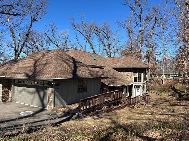 House with brown roof, stone and siding exterior, two-car garage, and wooden ramp, surrounded by bare trees.