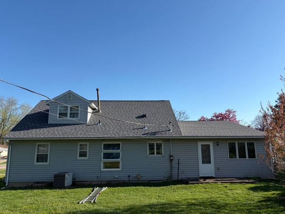 Brick house with white shutters and a black roof on a hill under a blue sky.