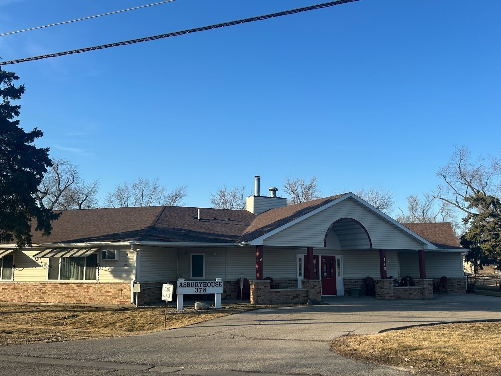 Brick house with white shutters and a black roof on a hill under a blue sky.