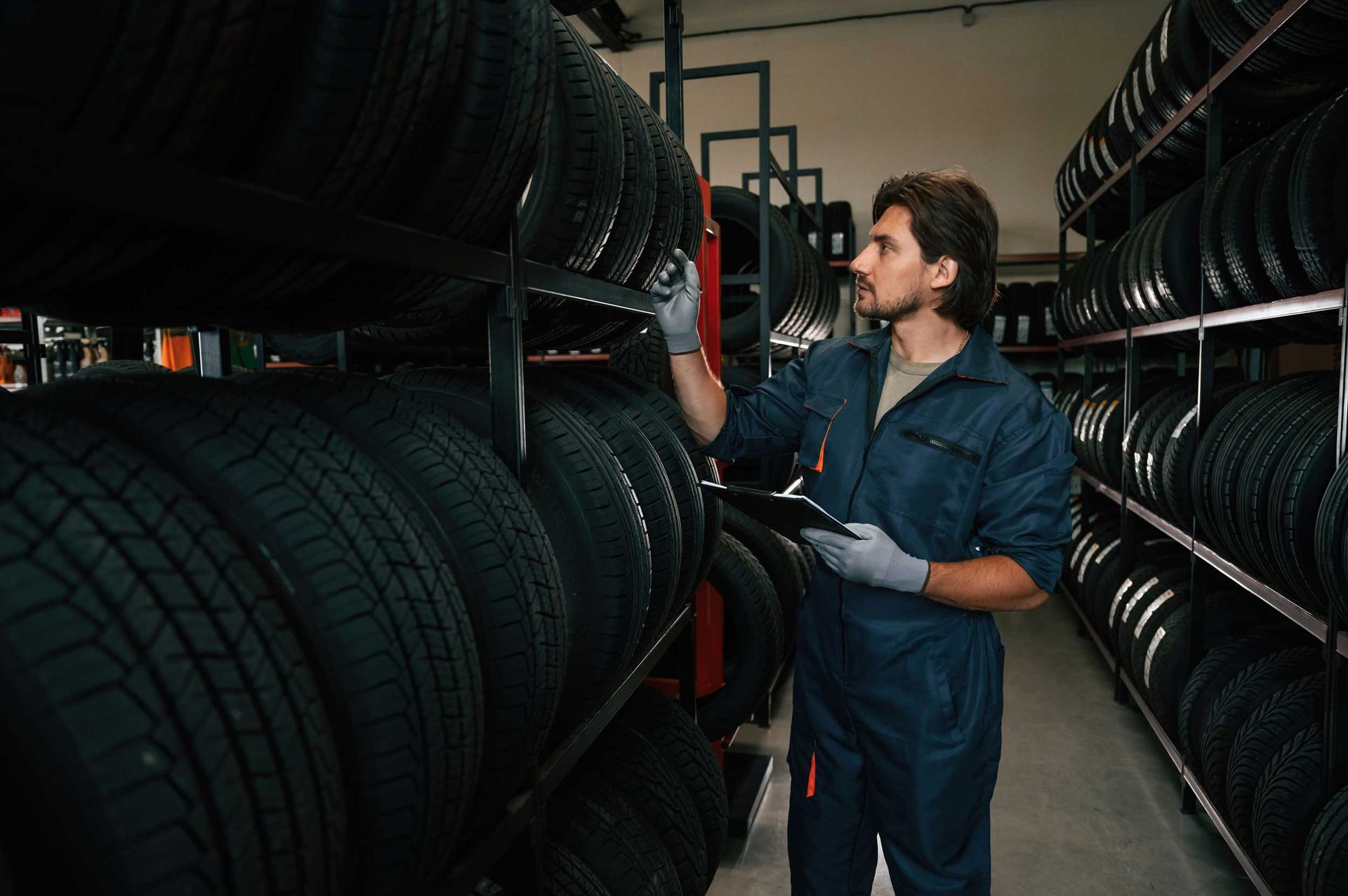 Worker checking and organizing tires on shelves in a storage area.