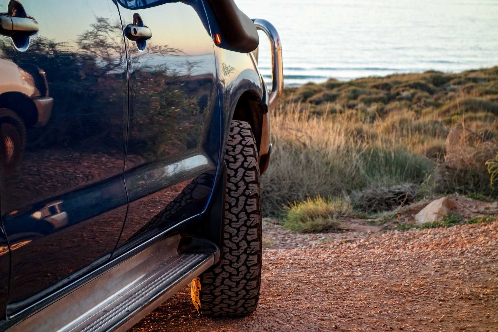 A 4WD vehicle with all-terrain tyres parked on a red dirt coastal track.