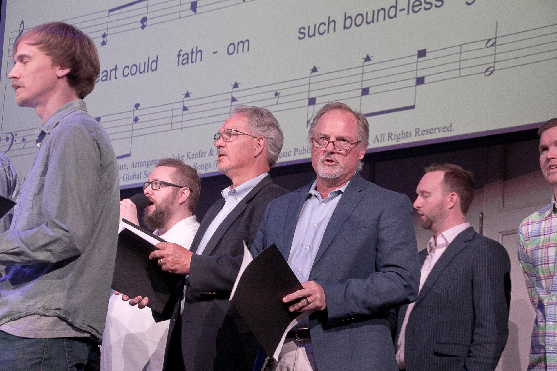 A group of men singing in front of a sheet of music that says such boundless