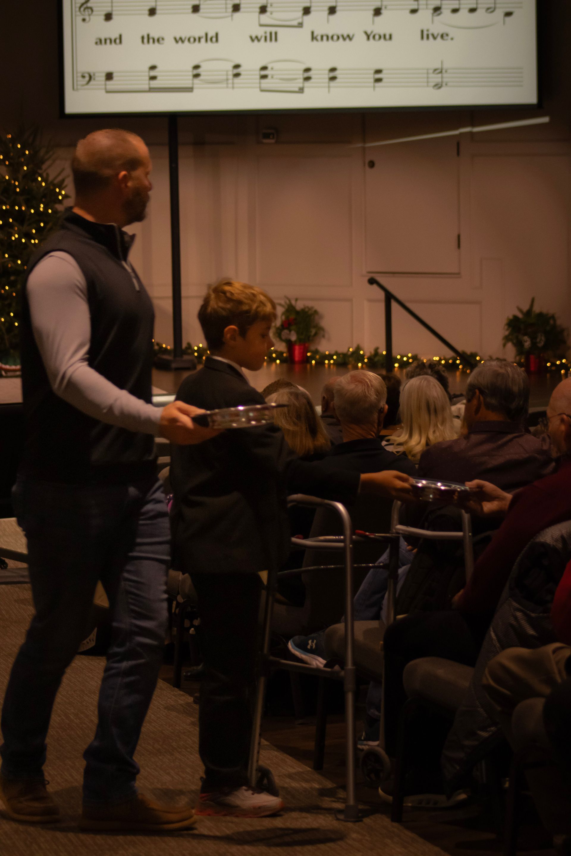 A man is standing next to a woman in a wheelchair holding a tray.