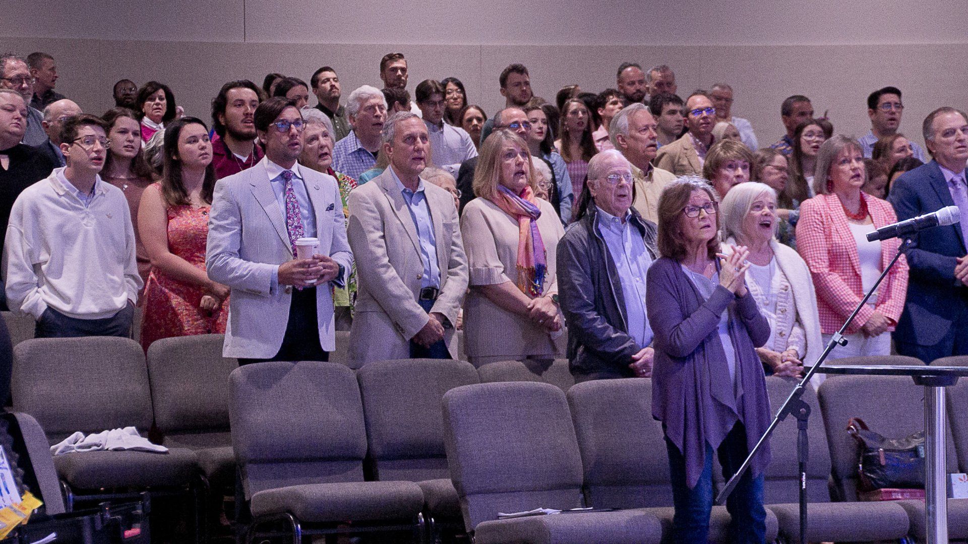A woman is singing into a microphone in front of a large group of people in a church.