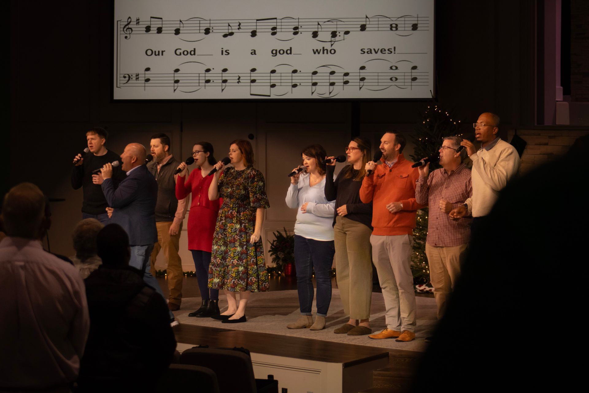 A group of people are standing on a stage singing into microphones.