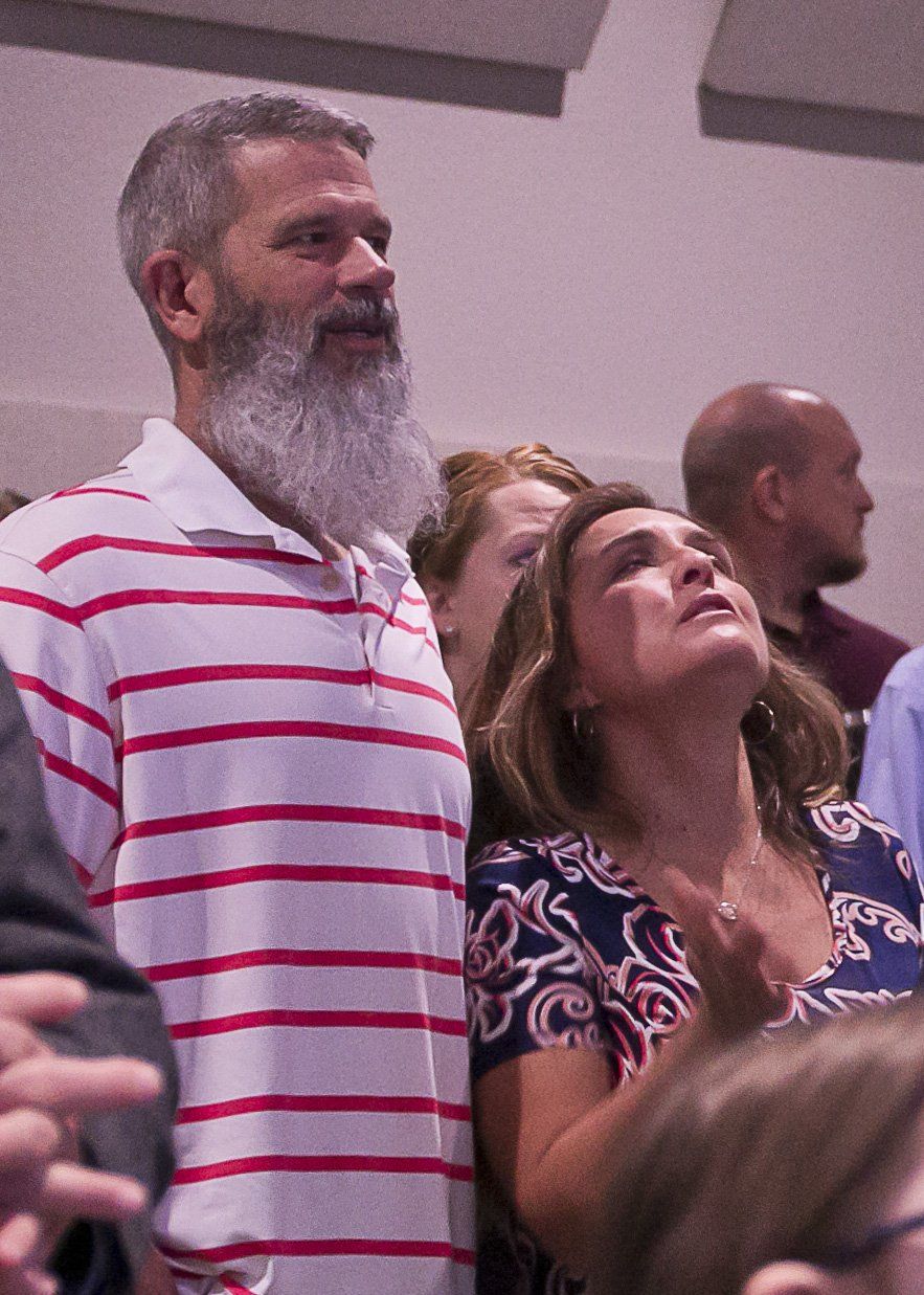 A man with a beard is standing in a crowd of people looking up.