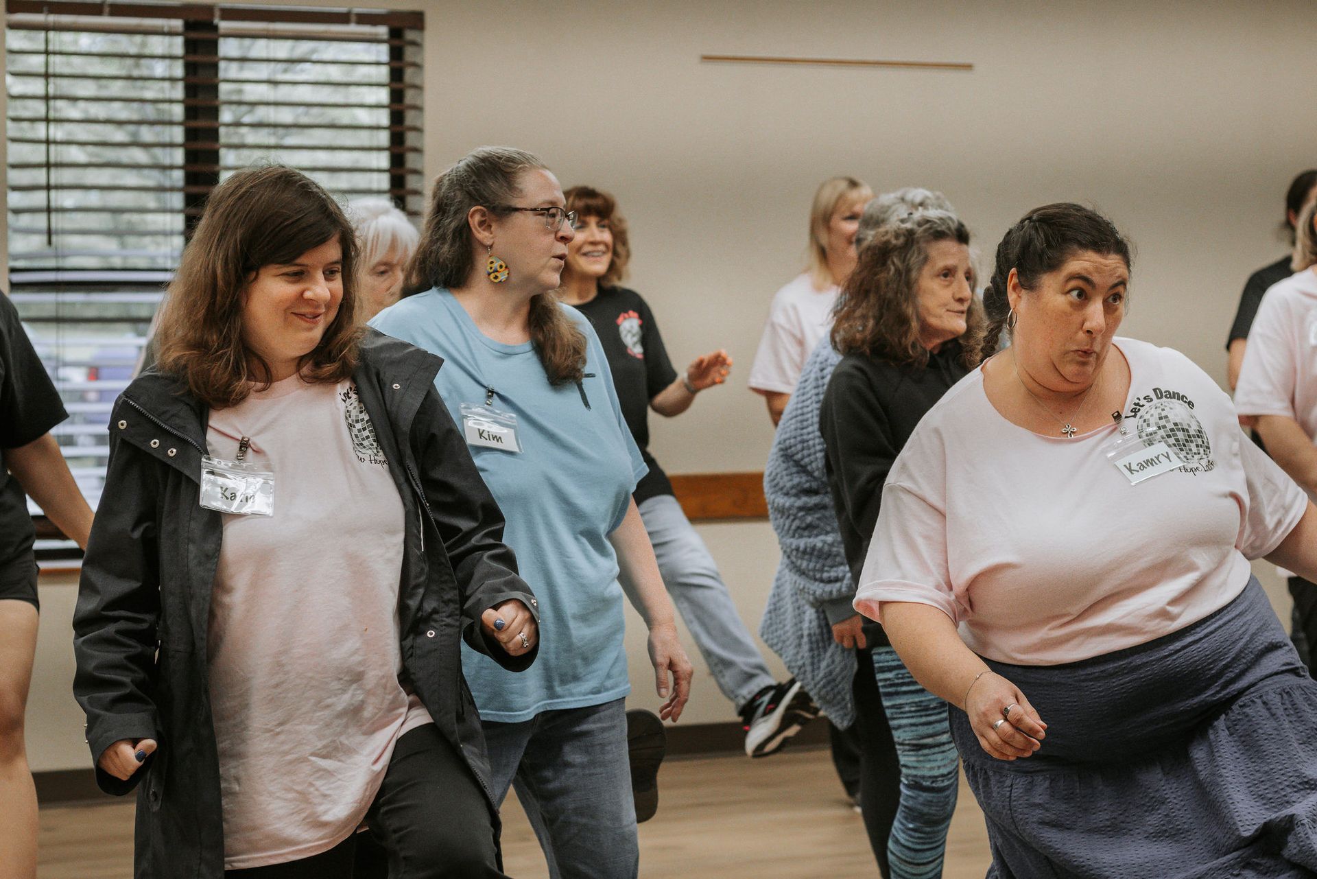 People dancing in a room. Diverse group with joyful expressions, dressed in casual clothing.