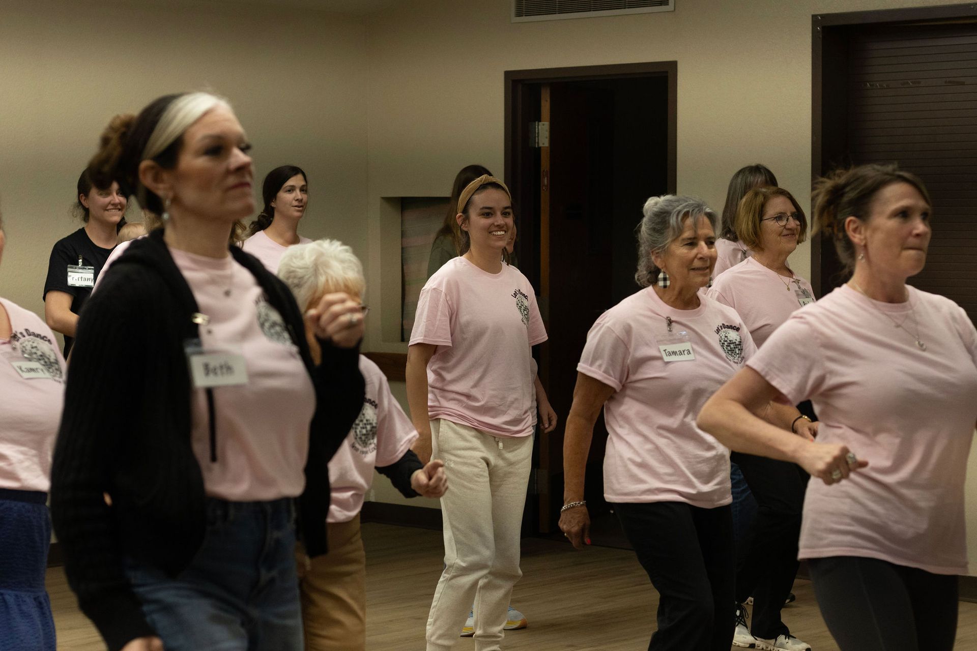 Group of women in pink shirts dancing indoors, smiling.