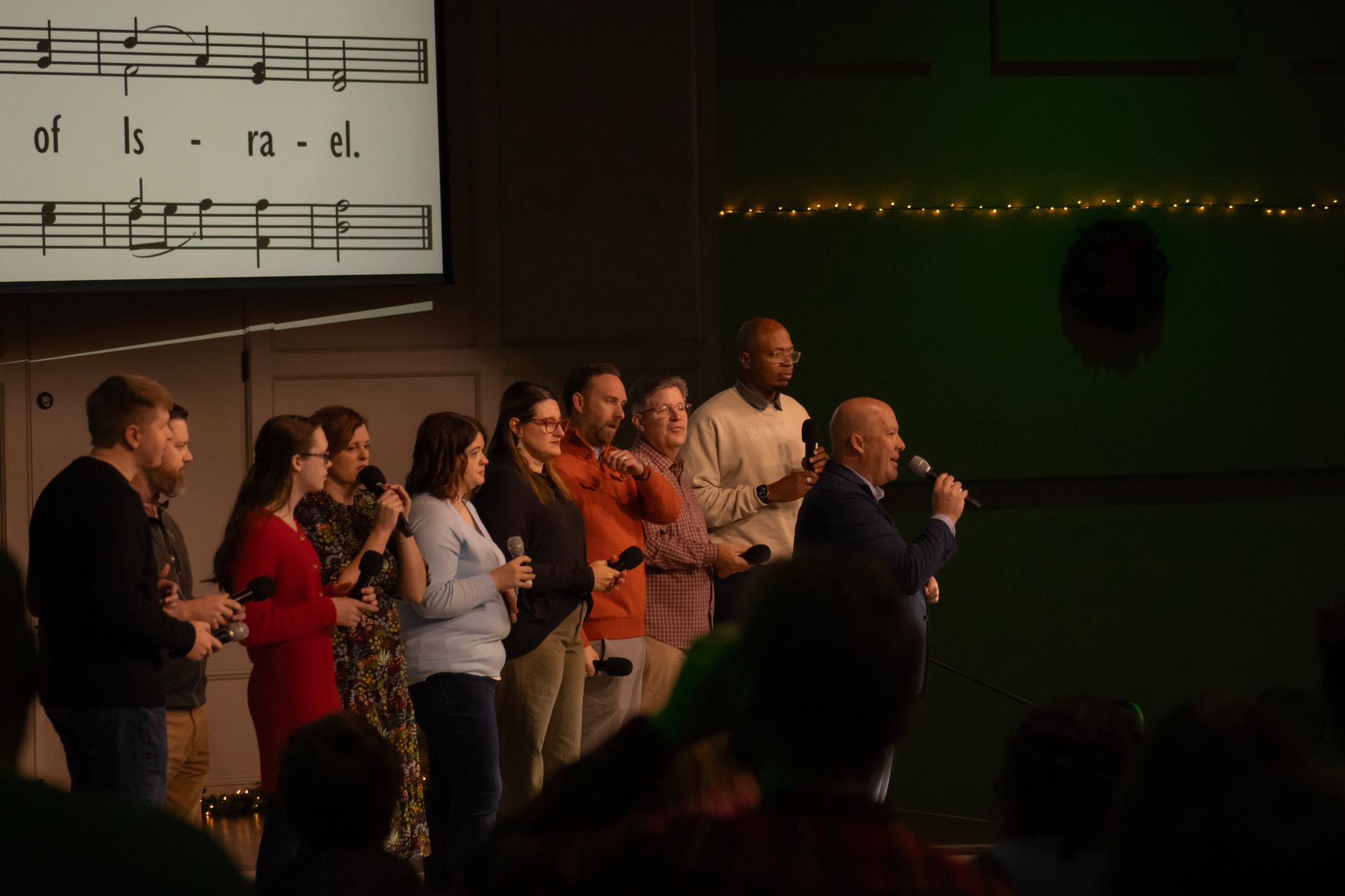 A group of people are singing in front of a large screen with music notes on it.