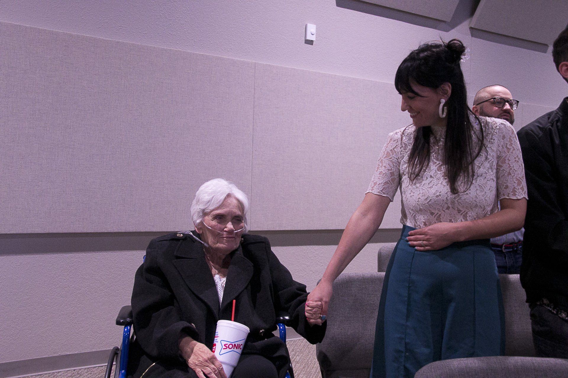 A woman is holding the hand of an older woman in a wheelchair.