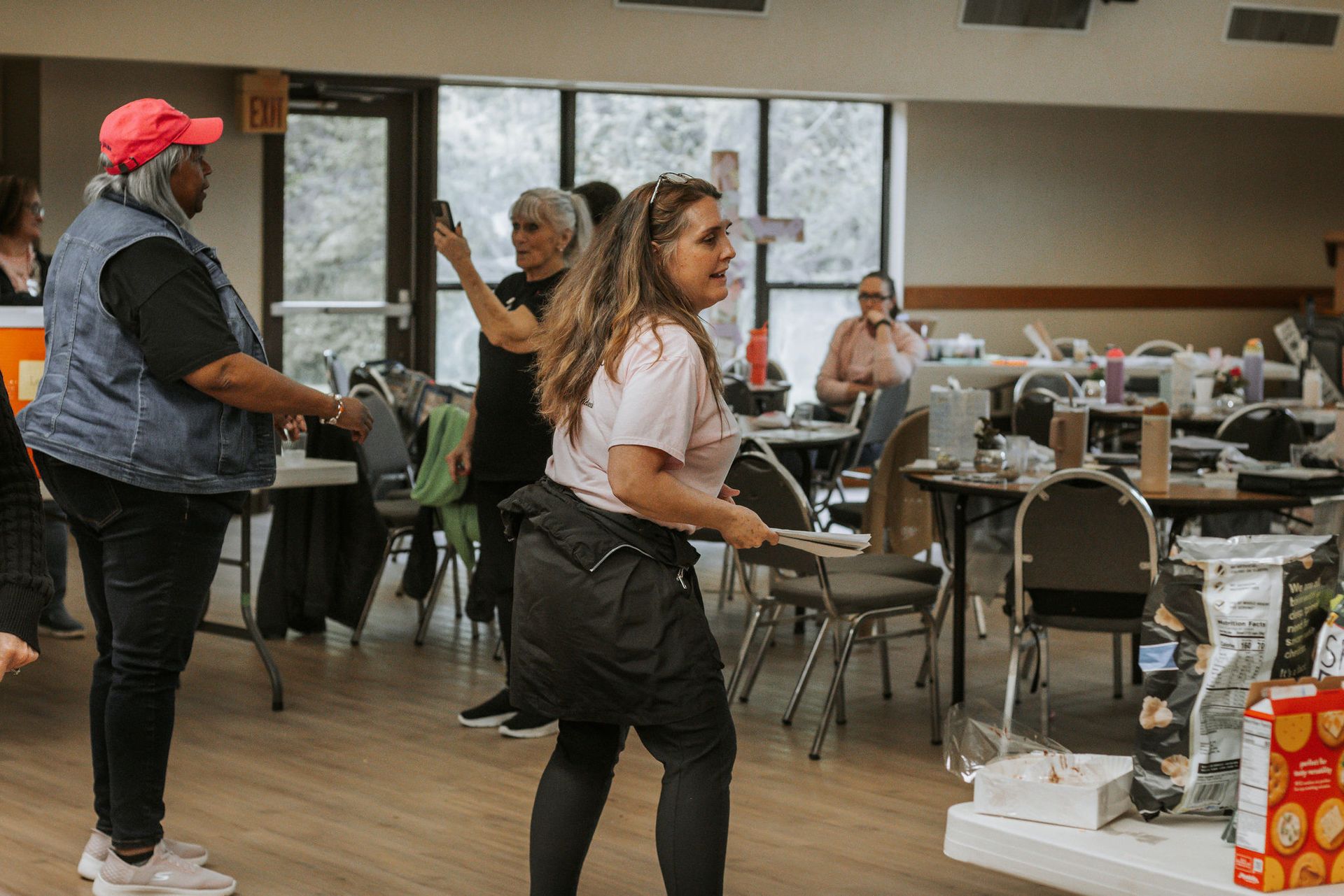 People at a community event, one woman carrying food, tables set up, and a window.