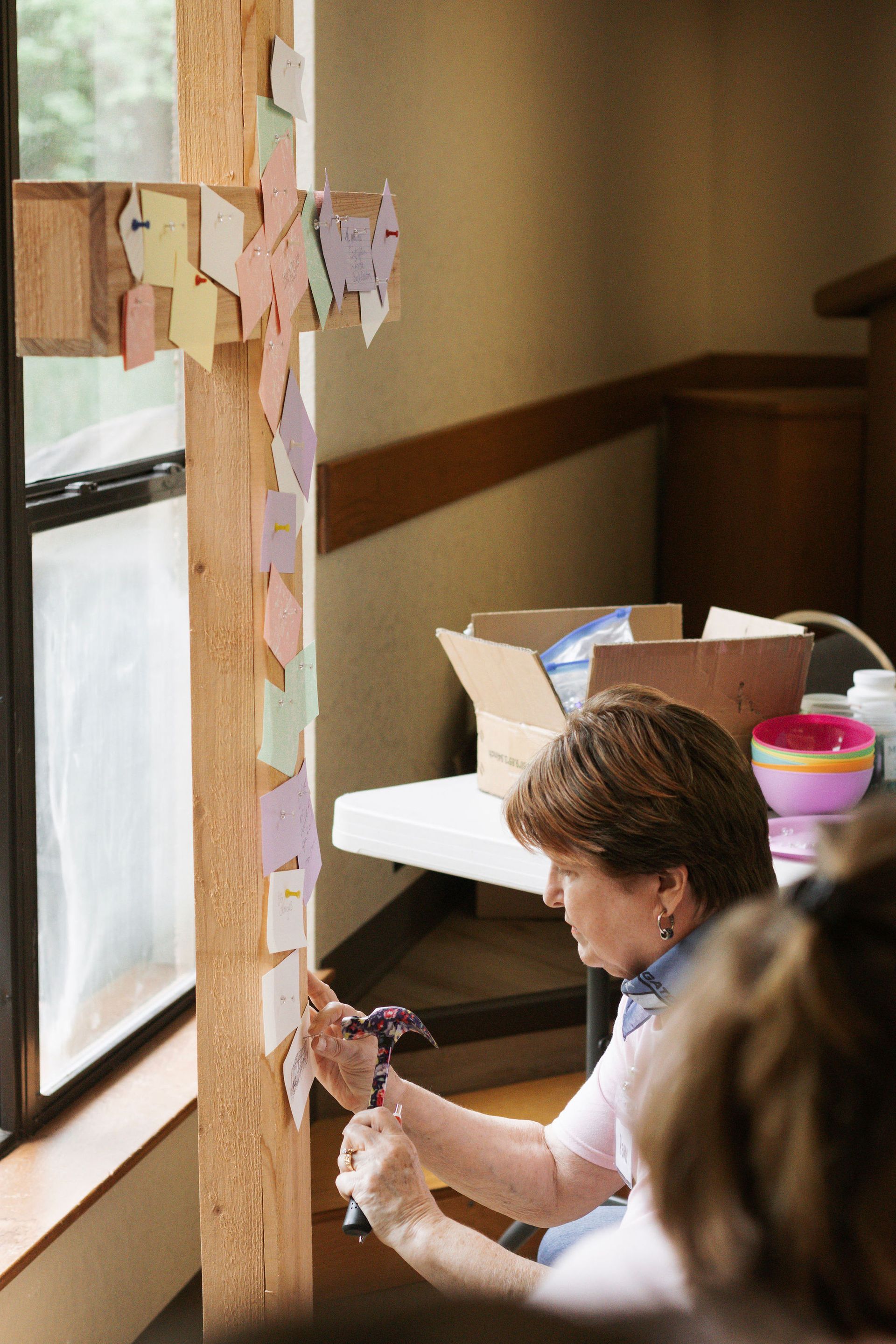 Woman attaching colorful paper leaves to a wooden cross inside a church.