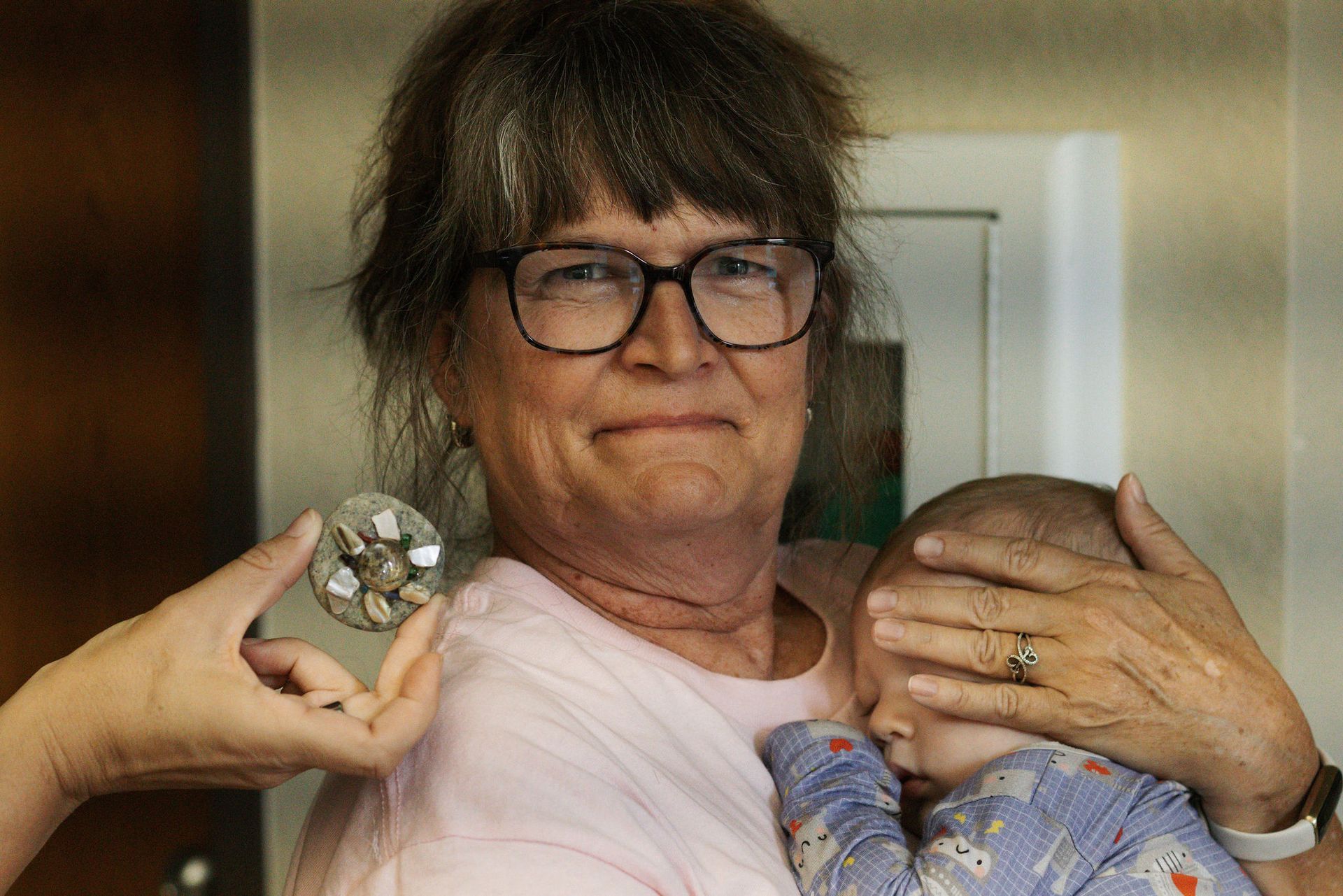 Woman holds a sleeping baby, while someone presents a jeweled object.
