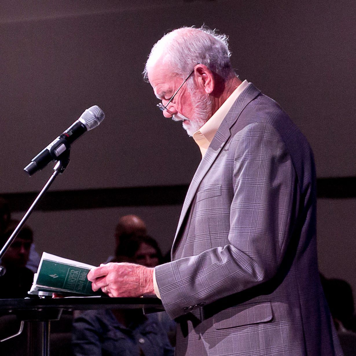 A man in a suit is reading a book in front of a microphone