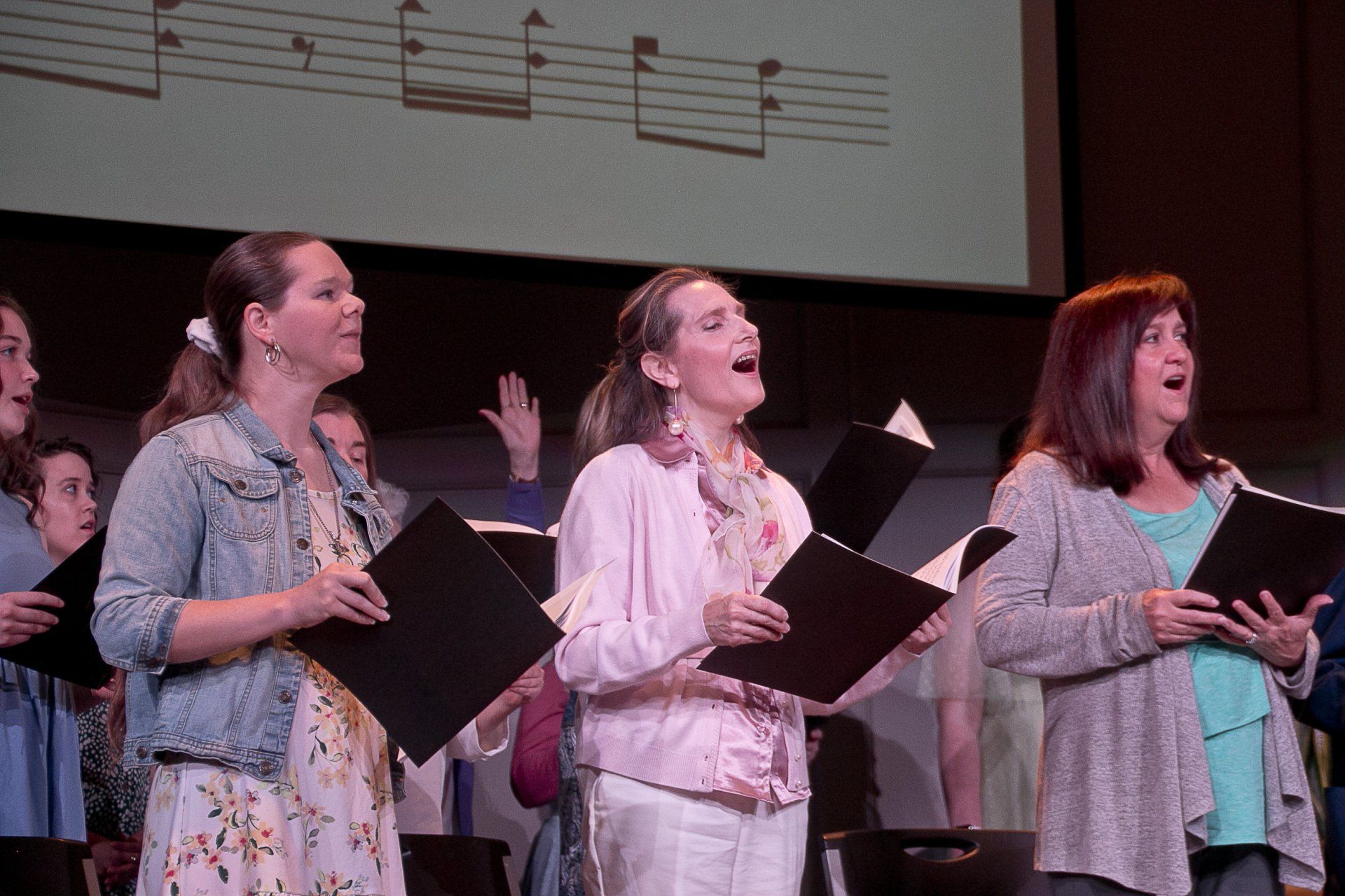 A group of women are singing in a choir on a stage.
