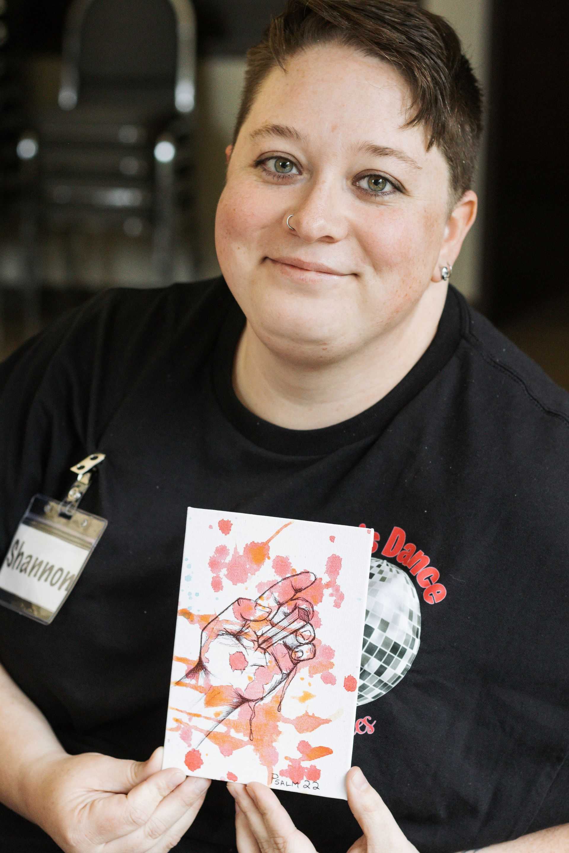 Woman with short hair, smiling, holding a colorful watercolor painting of a bird and flowers.