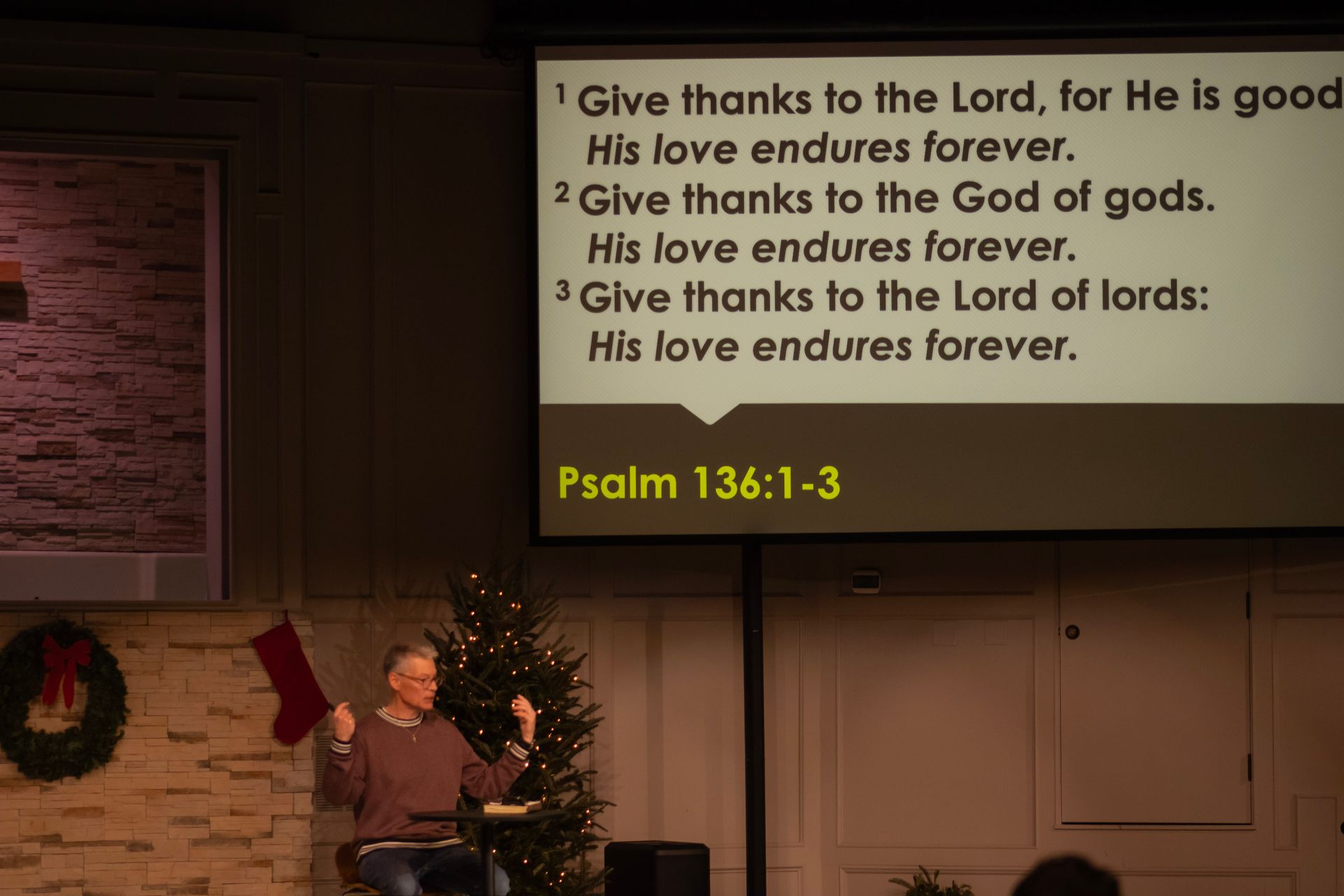 A man is giving a speech in front of a screen that says psalm 136 : 1-3