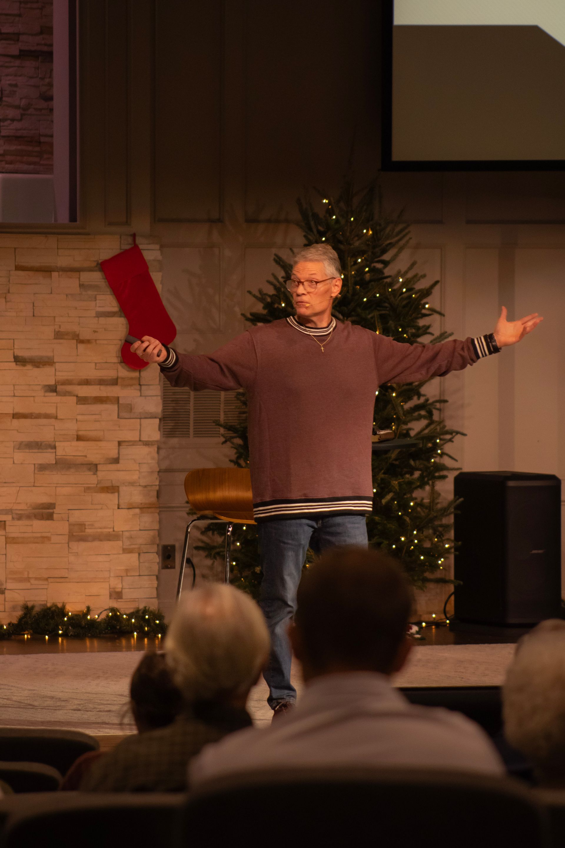 A man is holding a red christmas stocking in front of a christmas tree.