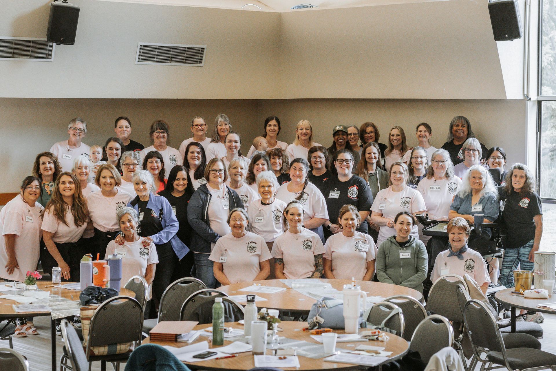 Group of women smiling, gathered around tables in a brightly lit room.