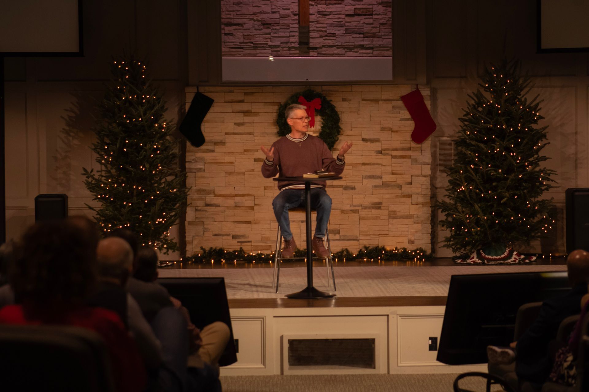 A man is sitting at a podium giving a speech in front of a christmas tree.