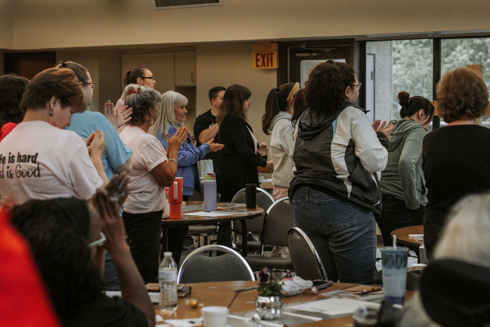 People clapping in a room with tables and chairs.  A sign for 