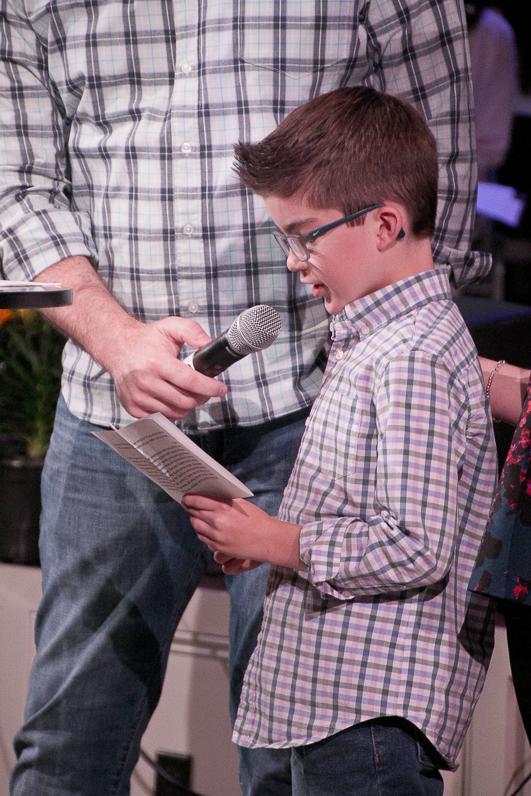 A young boy is holding a microphone and a piece of paper.
