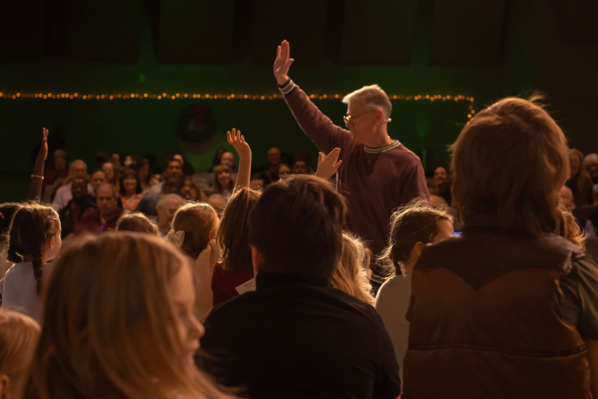 A man is standing in front of a crowd of people raising his hand in the air.