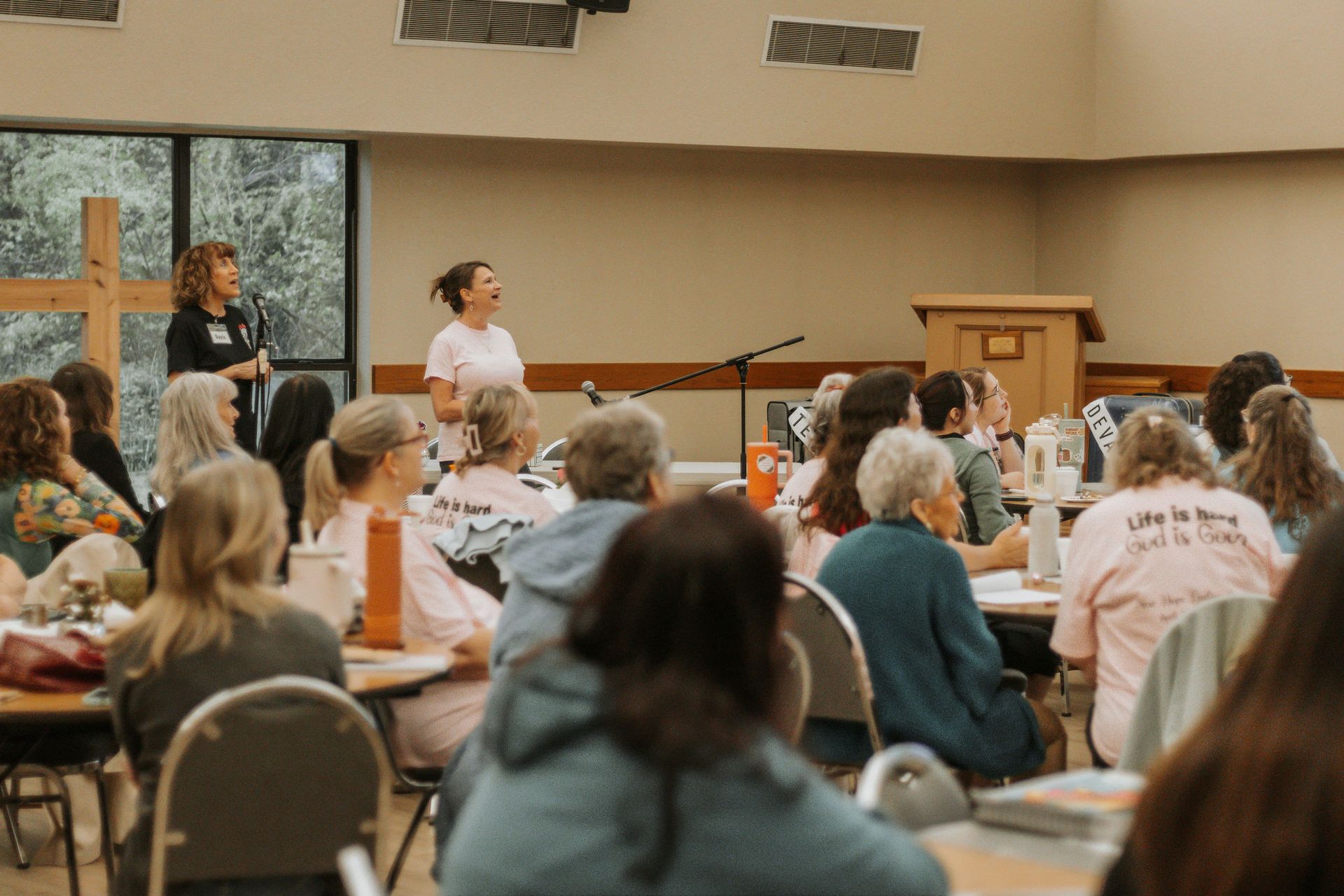 Women in a large room listen to two speakers at a podium.