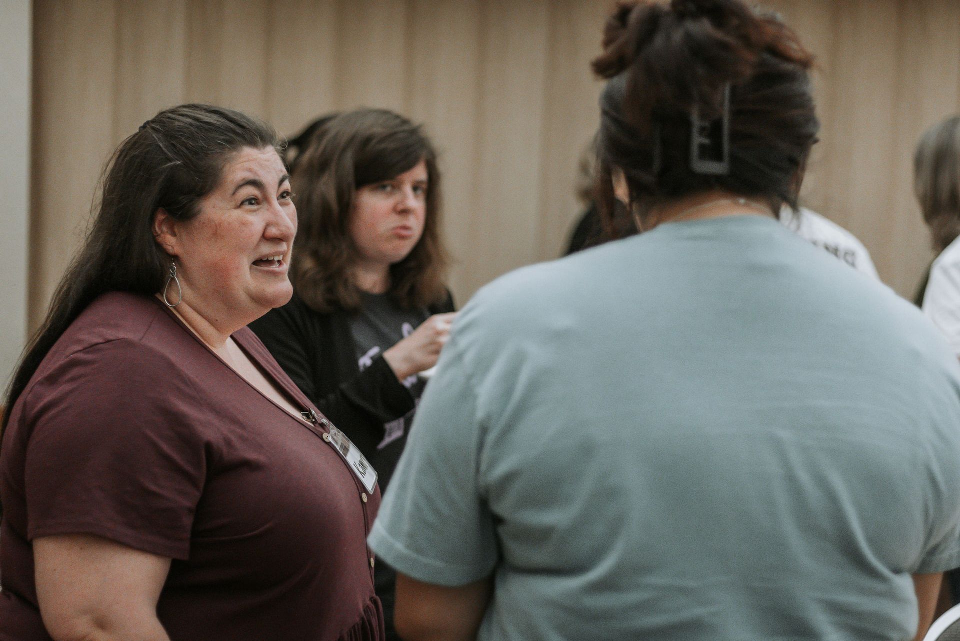 Three women in a room, two looking at each other, one has hair clip, all have expressions.